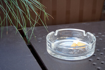 there are two cigarette butts in a round glass ashtray. an ashtray stands on a dark table in a cafe