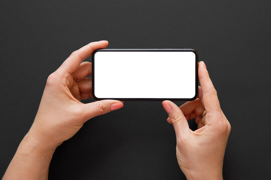 Person holding phone horizontally in both hands on dark background