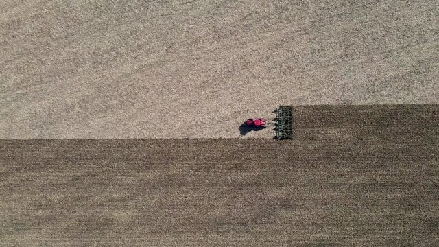 Aerial view of red tractor tilling center of farm field in the fall, sharp contrast shown on land. Driving horizontally across frame. North Dakota. Outdoors. 