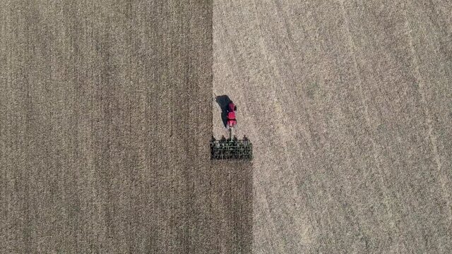 Aerial view of red tractor tilling center of farm field in the fall, sharp contrast shown on land. Driving vertically across frame. Drone zooms in. North Dakota. Outdoors. 