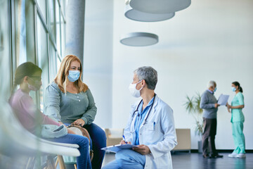 Worried mother with daughter talking to pediatrician at medical clinic during COVID-19 pandemic.