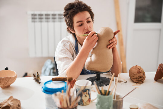 Attentive pottery artist using modeling tool for making clay figure