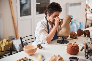 Accurate pottery shop employee shaping statue face with modeling knife