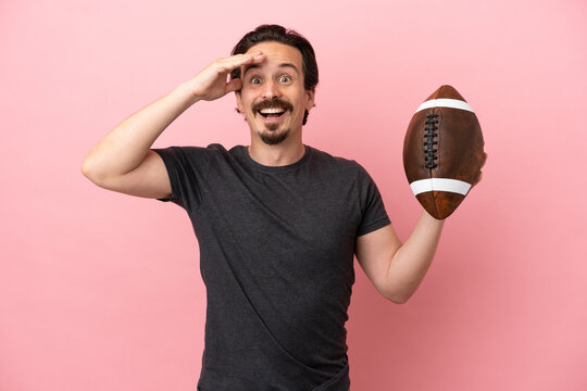 Young caucasian man playing rugby isolated on pink background with surprise expression