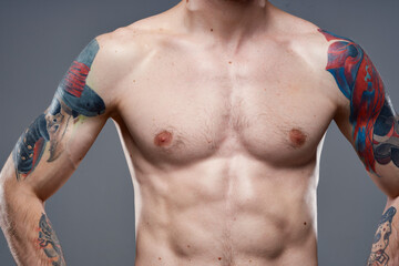 Fototapeta premium sporty man with pumped up abs tattoos on his arms gray background muscles