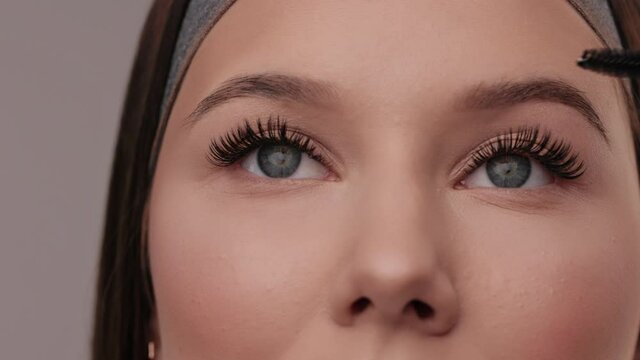 Close up portrait of woman face. Young, beautiful girl with fresh soft skin combing long black eyelashes with special mascara brush. Fake eyelashes. Eyelashes extensions close up.