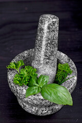 fresh herbs in a stone mortar on a black wooden table