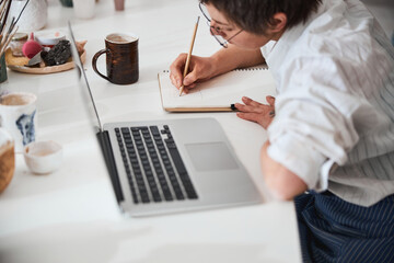Focused worker bending over notepad while writing with pencil