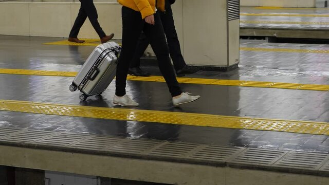 Traveler woman walk with trolley case at railway station, slow motion tracking shot. Low half view of legs and platform, male passengers walk on background