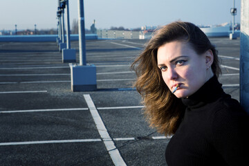 young brunette woman smoking a cigarette outdoors at a parking deck
