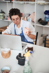 Potter holding beige cup while staring in laptop display