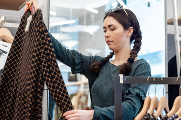 Portrait of a young Caucasian woman looking for clothes in a store. The concept of consumerism