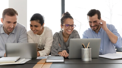 Happy diverse colleagues working on project together, brainstorming, using laptop, looking at...