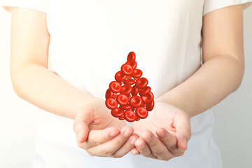 Blood donation. Human hands holding blood drop shape of red blood cells over white background....