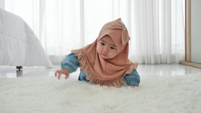 Baby girl asian ethnicities 6 months old in traditional hijab clothing crawling on floor slow motion. Little child playing in white sunny bedroom