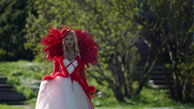 fantasy image of red queen, blonde woman in red gorgeous dress is walking in garden
