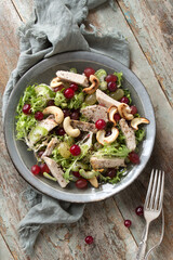 flat lay of plate with chicken breast, grapes, cashew and cranberry salad on wooden table