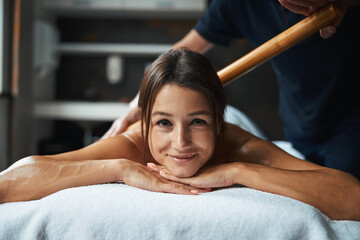 Brunette elegant female receiving manual massage therapy with wooden tool in wellness center