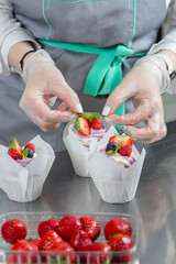 Woman hands chef decorating Cupcakes with pink butter cream and fresh berries