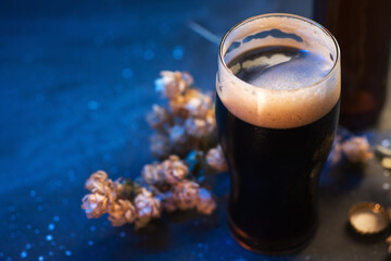 A glass of dark craft beer on the table. Dry hop branch, blue background light copy space