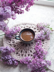Obraz na płótnie Canvas Ceramic blue espresso coffee cup on a knitted napkin, a bouquet of blooming lilacs . Springtime vertical postcard