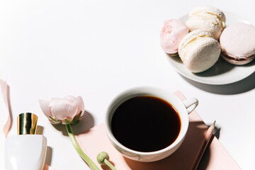 Fototapeta na wymiar cup of coffee, pink flowers, perfume and macaroons on white background, top view