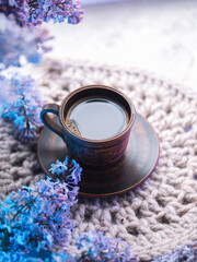 Fototapeta na wymiar A clay cup of espresso coffee on a knitted napkin, a bouquet of blooming lilacs . Springtime vertical postcard