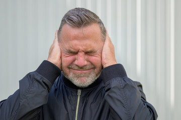 Portrait of an exhausted middle-aged man covering his ears