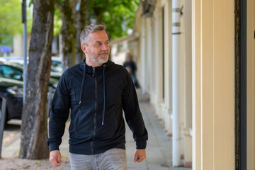 Middle-aged man in leisurewear walking down an urban street - Powered by Adobe