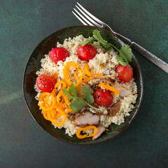 flat lay bowl of couscous with turkey, cherry tomatoes and peppers on a dark table, space for text