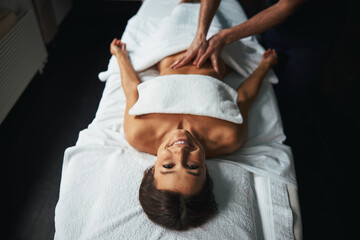 Positive joyful lady feeling great while unrecognized male masseur stroking client body in spa salon