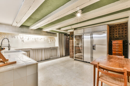 Contemporary Big Kitchen Of Mansion House With Stainless Fridge And Wooden Wine Racks Under White Beams Of Ceiling