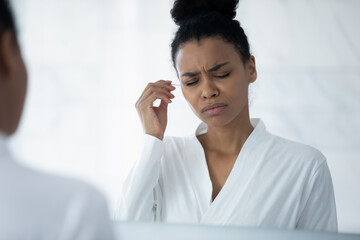 Upset Black girl feeling discomfort, pain while cleaning ears with cotton swab from earwax, hurting earbud, getting damage or infection during health risky hygienic procedure. Healthcare concept