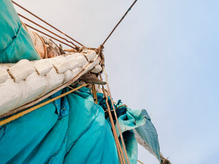 A fragment of a white wooden mast and a turquoise sail of a felucca boat. Bottom view, against the background of the sky. - obrazy, fototapety, plakaty