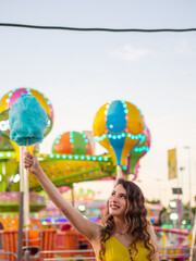 Obraz na płótnie Canvas Mujer joven disfrutando de un algodón de azúcar en la feria o parque de atracciones