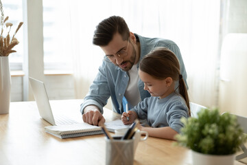 Loving young Caucasian father study together with little daughter use laptop gadget at home. Caring dad help small girl child with homework assignment, have online webcam lesson on computer.