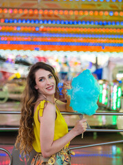 Mujer joven disfrutando de un algodón de azúcar en la feria o parque de atracciones