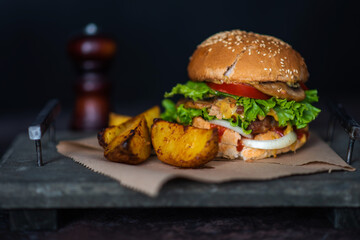Tasty grilled homemade beef burger, tomato, cheese, cucumber and lettuce with french fries on a wooden background. Burger on the board on a dark background.