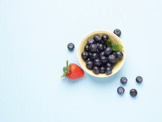 Bowl of fresh blueberries and a strawberry on a blue background