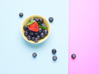 Bowl of fresh blueberries and a strawberry on a blue and pink background