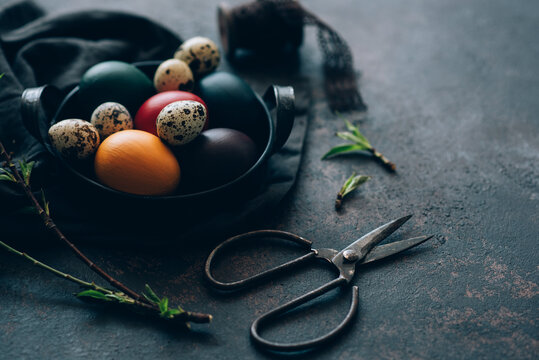 Vintage iron tray full of colorful Easter eggs with hay and spring branch on a dark rustic background. Copy space.