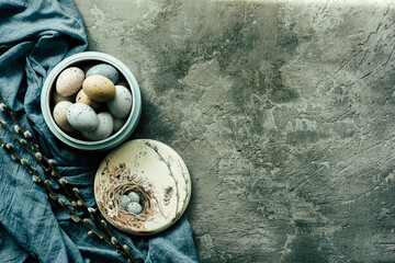Vintage background with easter eggs in wooden plate on a concrete background. Napkin and spring branches. Top view with copy space.