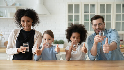 Portrait of young multiracial family with two children drink clean still mineral water together in...
