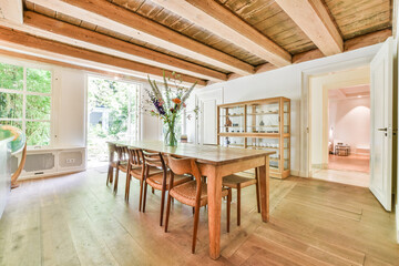 Wooden dining table with chairs under ceiling with wooden beams in cozy country room of house