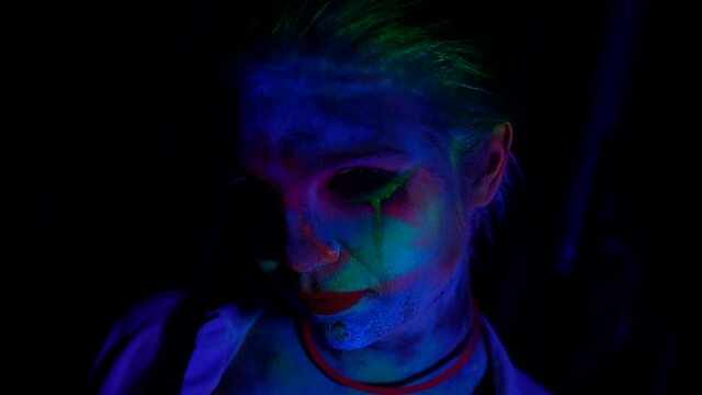closeup of face of young woman with scary makeup by fluorescent paints, female portrait in darkness