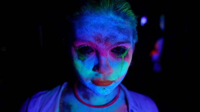 gloomy young woman with fluorescent makeup, portrait in UV lights in darkness