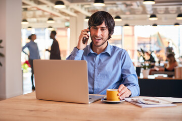 Businessman Sitting At Desk On Phone Call In Modern Open Plan Office