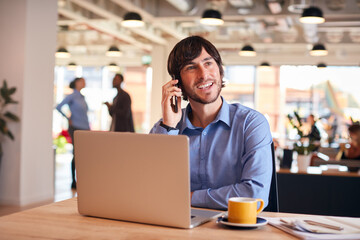 Businessman Sitting At Desk On Phone Call In Modern Open Plan Office