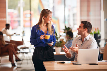 Businessman And Businesswoman Having Informal Meeting By Desk In Modern Open Plan Office