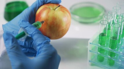 Female hands in medical gloves make an injection into an apple close-up. Healthy and unhealthy food, GMO, chemistry. 4K UHD - Powered by Adobe